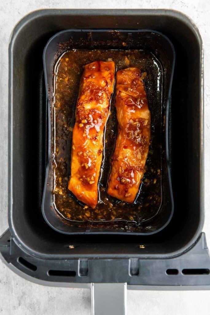 Two strips of marinated salmon in the air fryer pan.