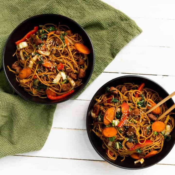 Two bowls of instant pork lo mein on a green cloth in the background.