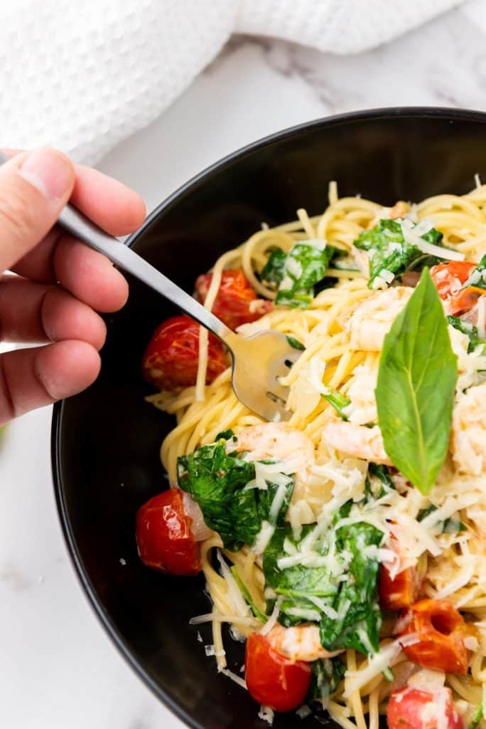 A person holding fork on spaghetti scampi e Spinaci with basil on top.