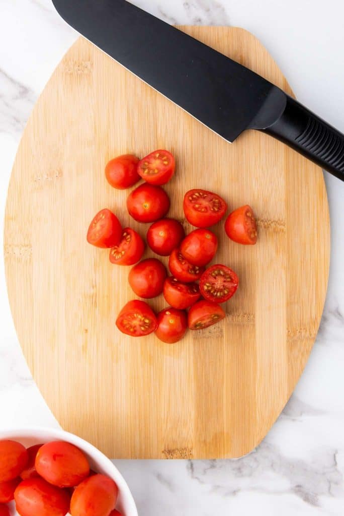 Half cherry tomatoes on chopping board and knife in the side.