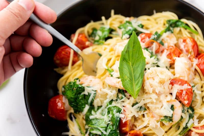 A person holding fork on spaghetti scampi e Spinaci with basil on top.