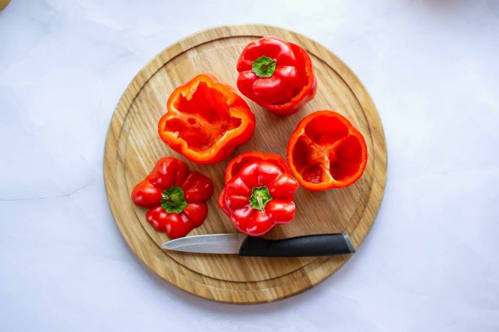 Cut off bell peppers on a wooden board with a knife.