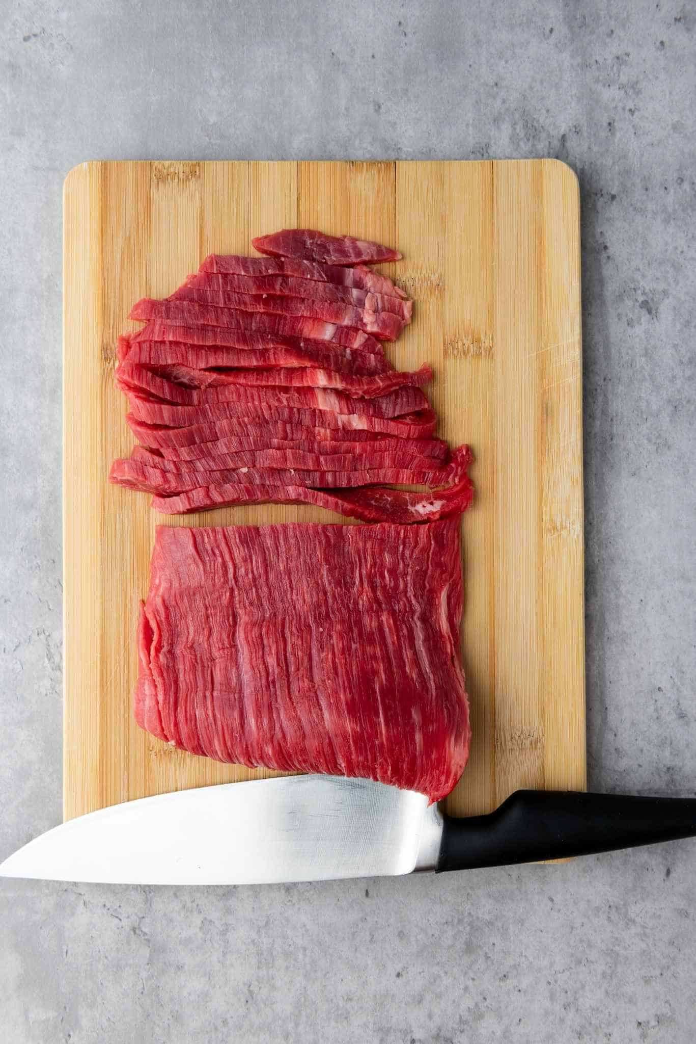 Flank steak cut into thin strips on a wooden board.