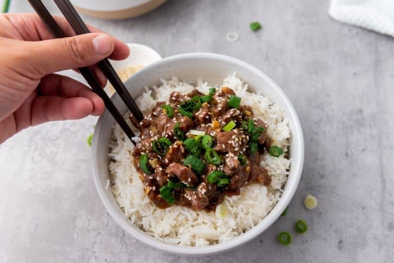 A person holding chopstick on a slow cooker Mongolian beef food.