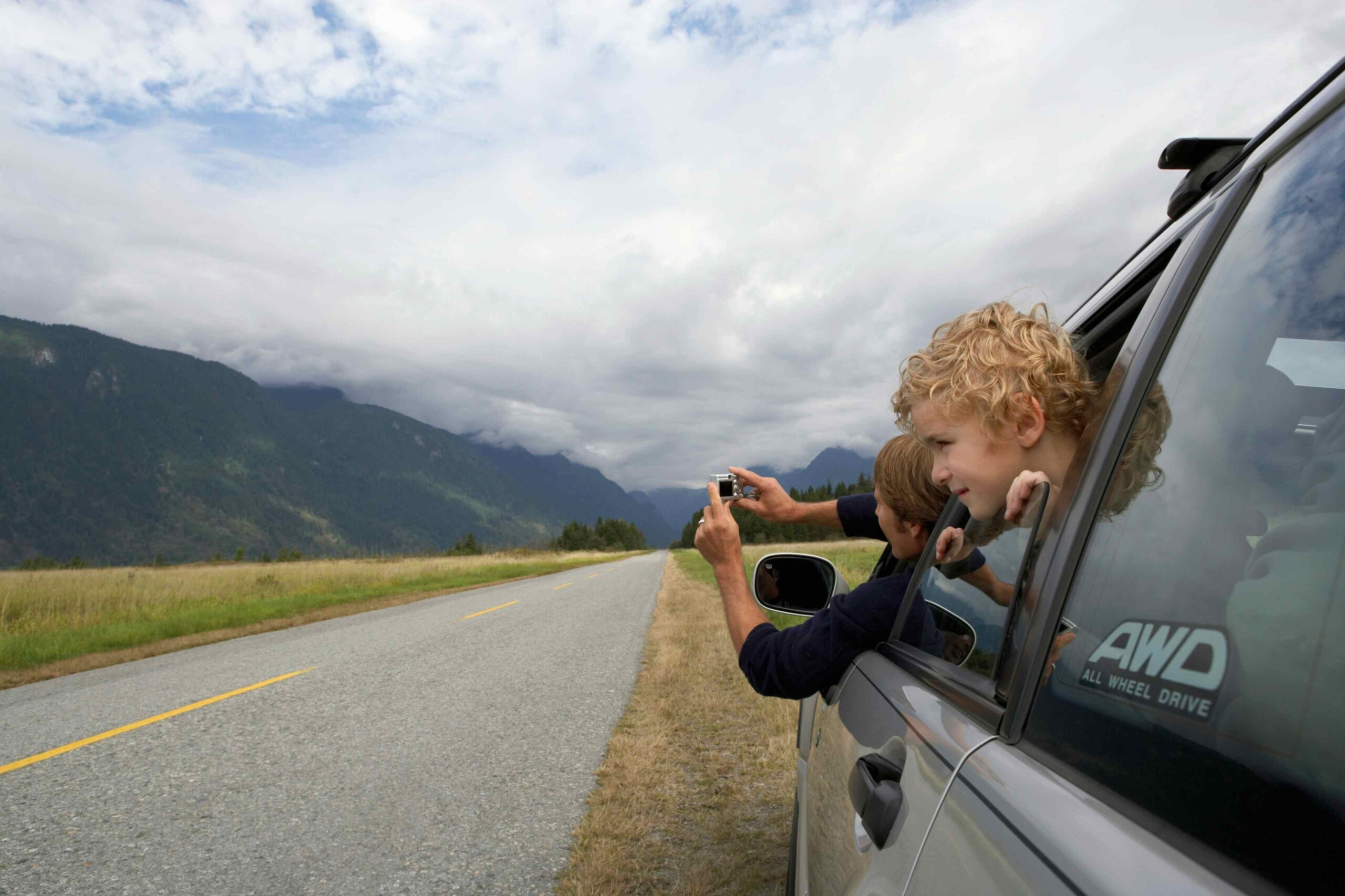 A person leaning out of driving car window to take a photo.