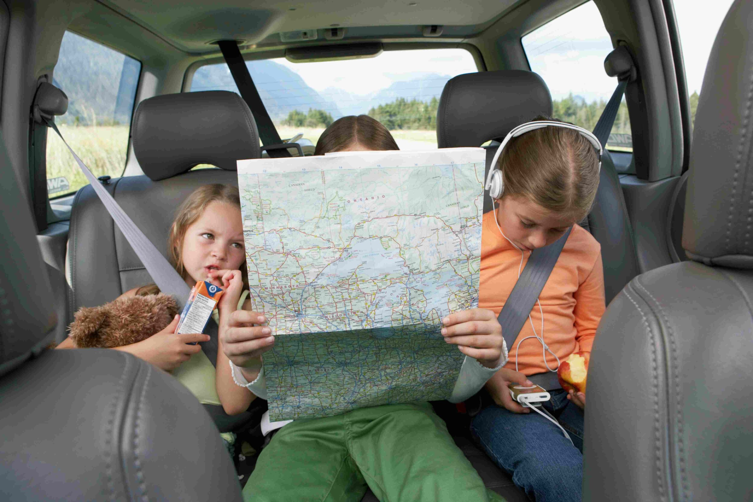 Three children looking at a map in the car.