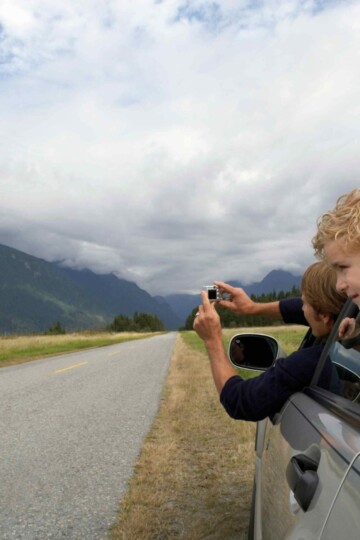 A person leaning out of driving car window to take a photo.