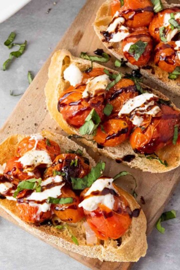 A plate of Roasted Cherry Tomato and Burrata Bruschetta garnished with fresh basil and drizzled with balsamic glaze.