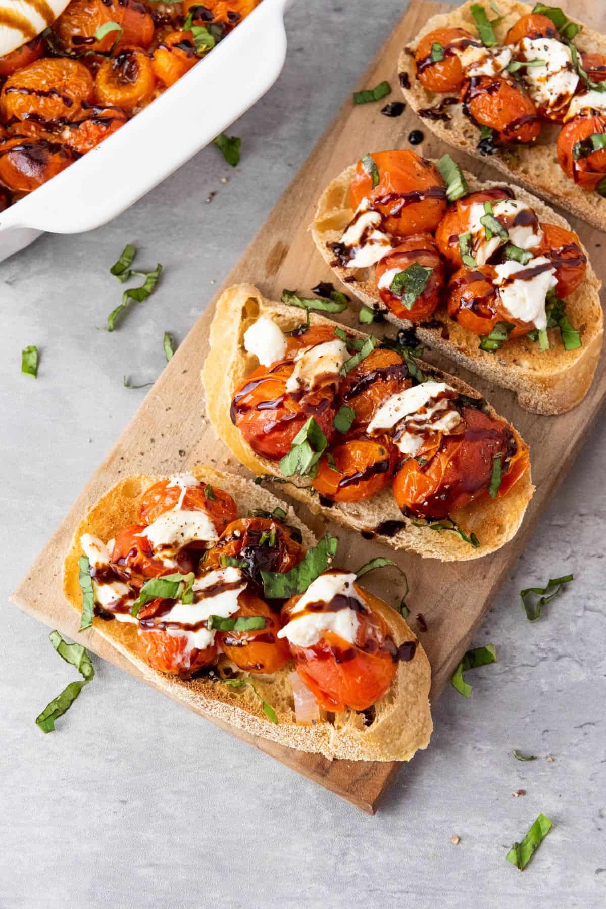 Served roasted cherry tomato and burrata bruschetta in a wooden board.