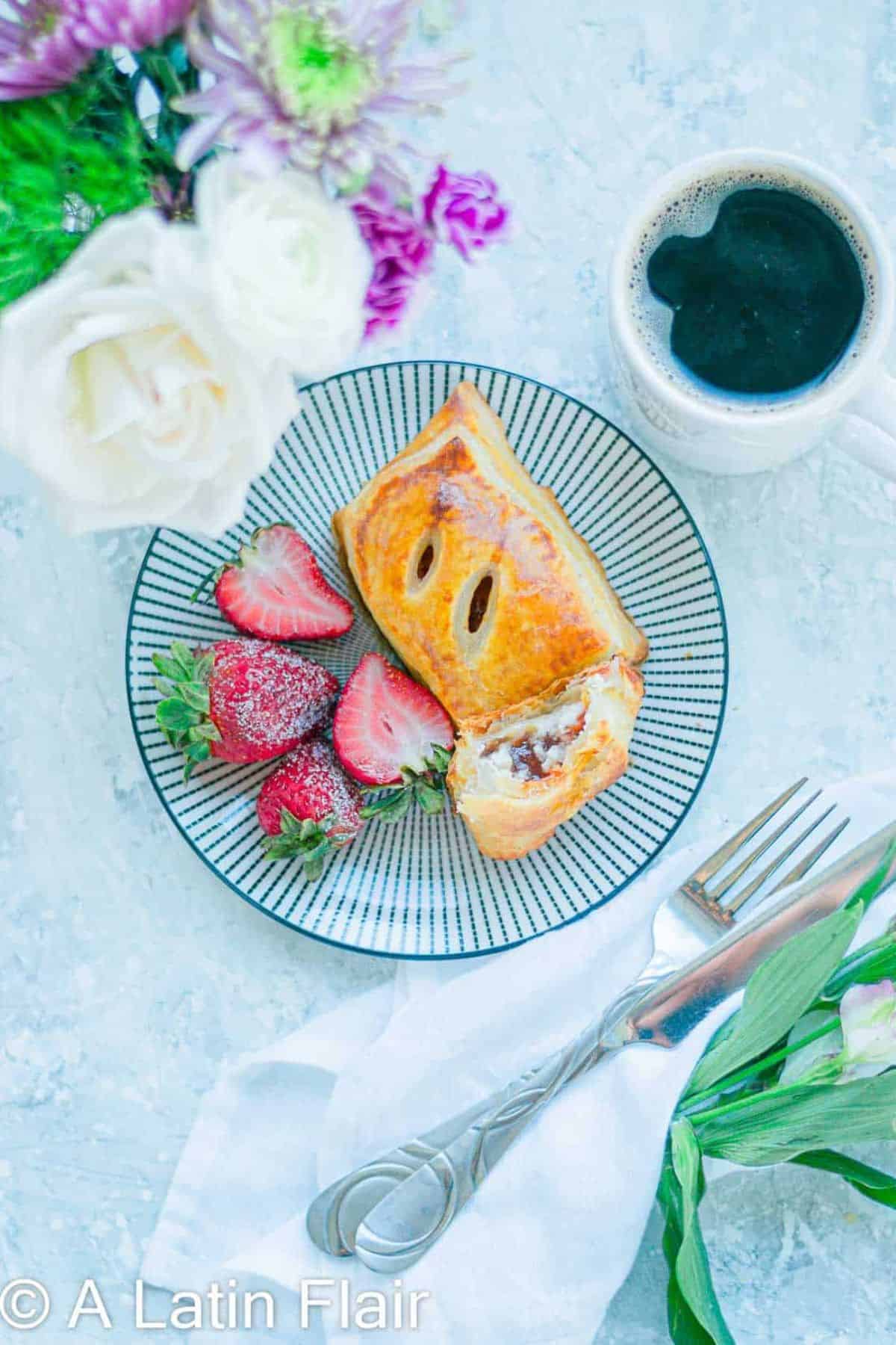 A piece of guava and cheese pastry on a plate with fresh strawberries on its side.