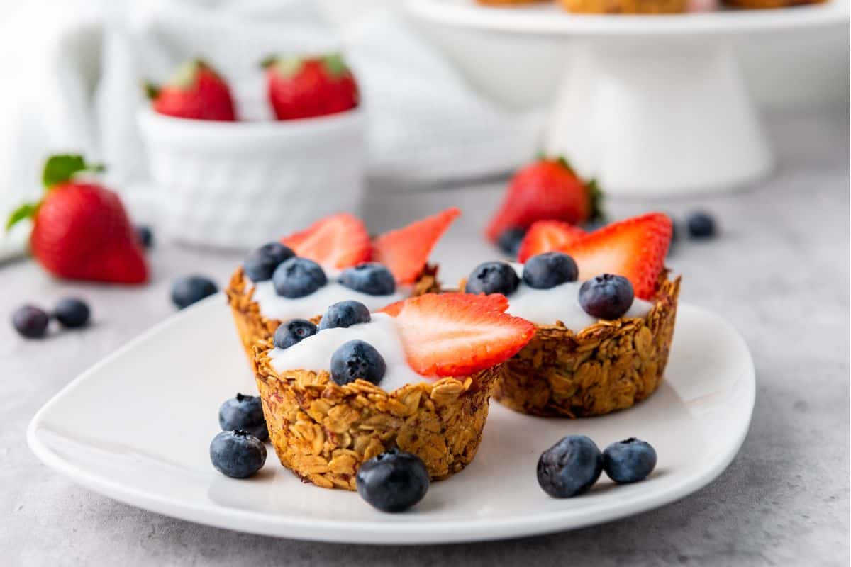 Close-up of three mini granola cups filled with creamy yogurt and topped with fresh berries, elegantly arranged on a plate.