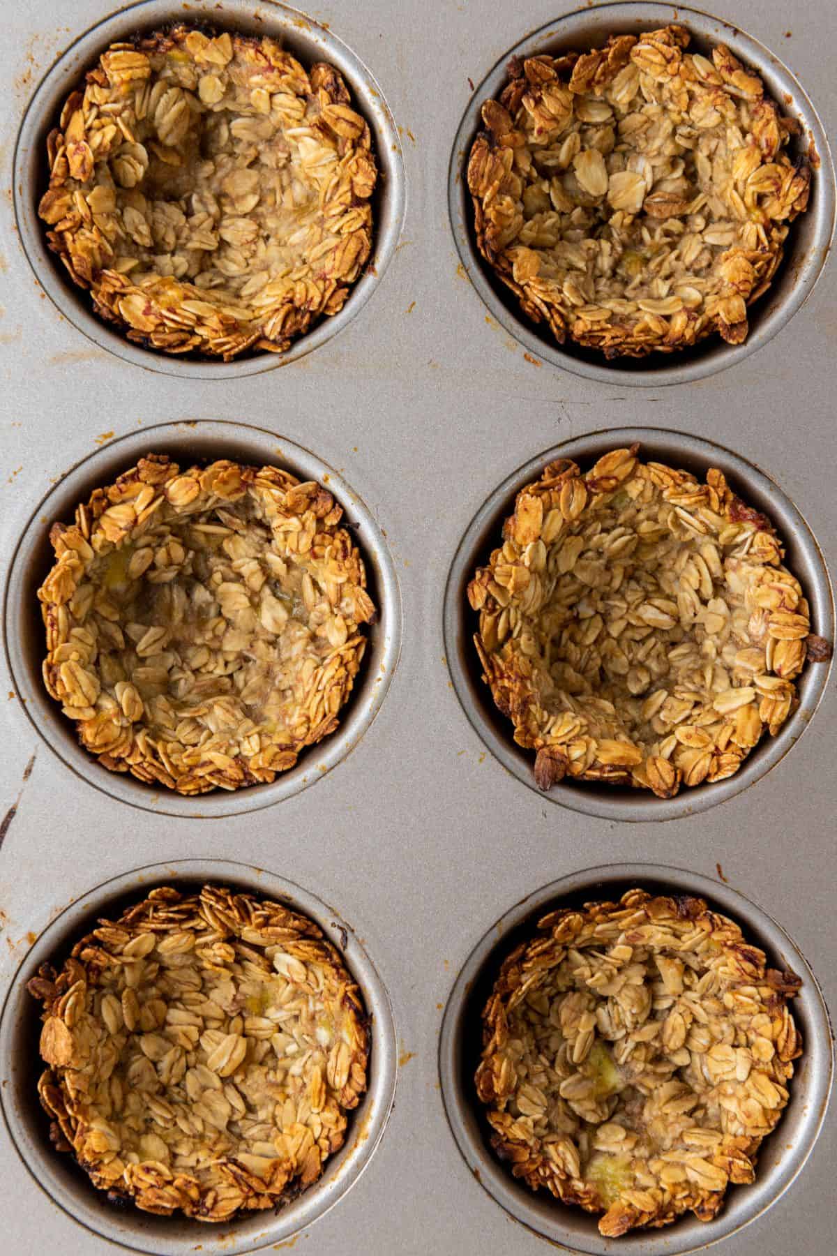 Granola mixture being spooned into a muffin pan, pressed into cup shapes for baking.