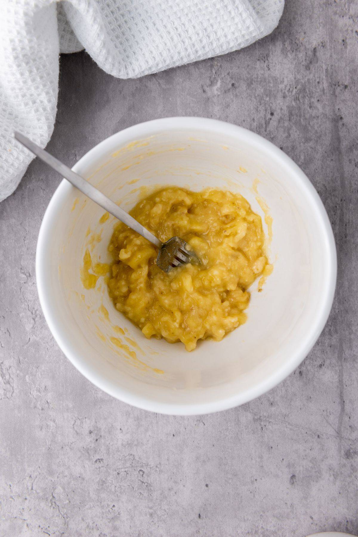 Mashed banana in a bowl with a fork, showing a soft and creamy texture ready for mixing.