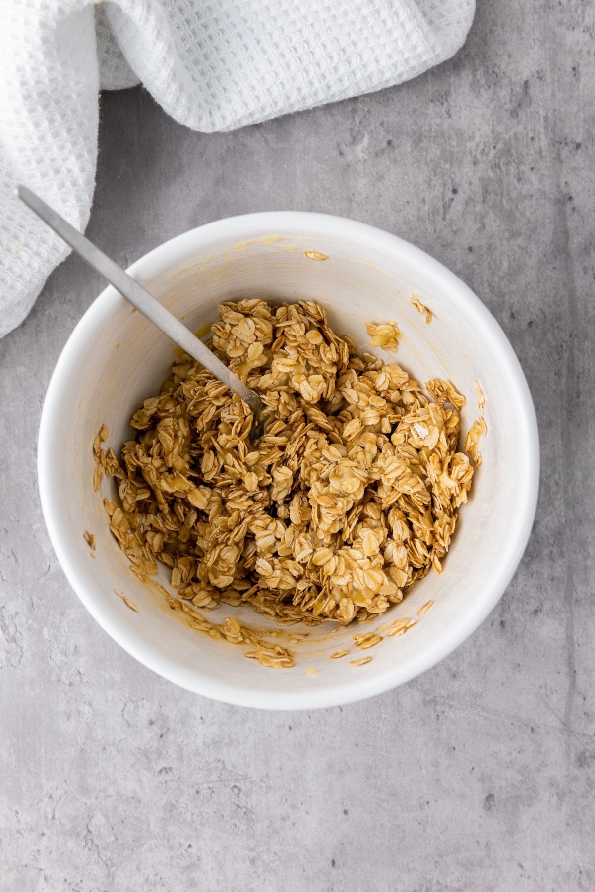 Granola mixture being stirred in a bowl with oats, honey, and mashed banana, combining all the ingredients together.