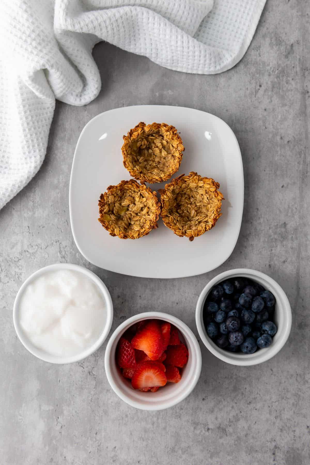 Freshly baked granola cups in a muffin pan, surrounded by ingredients.