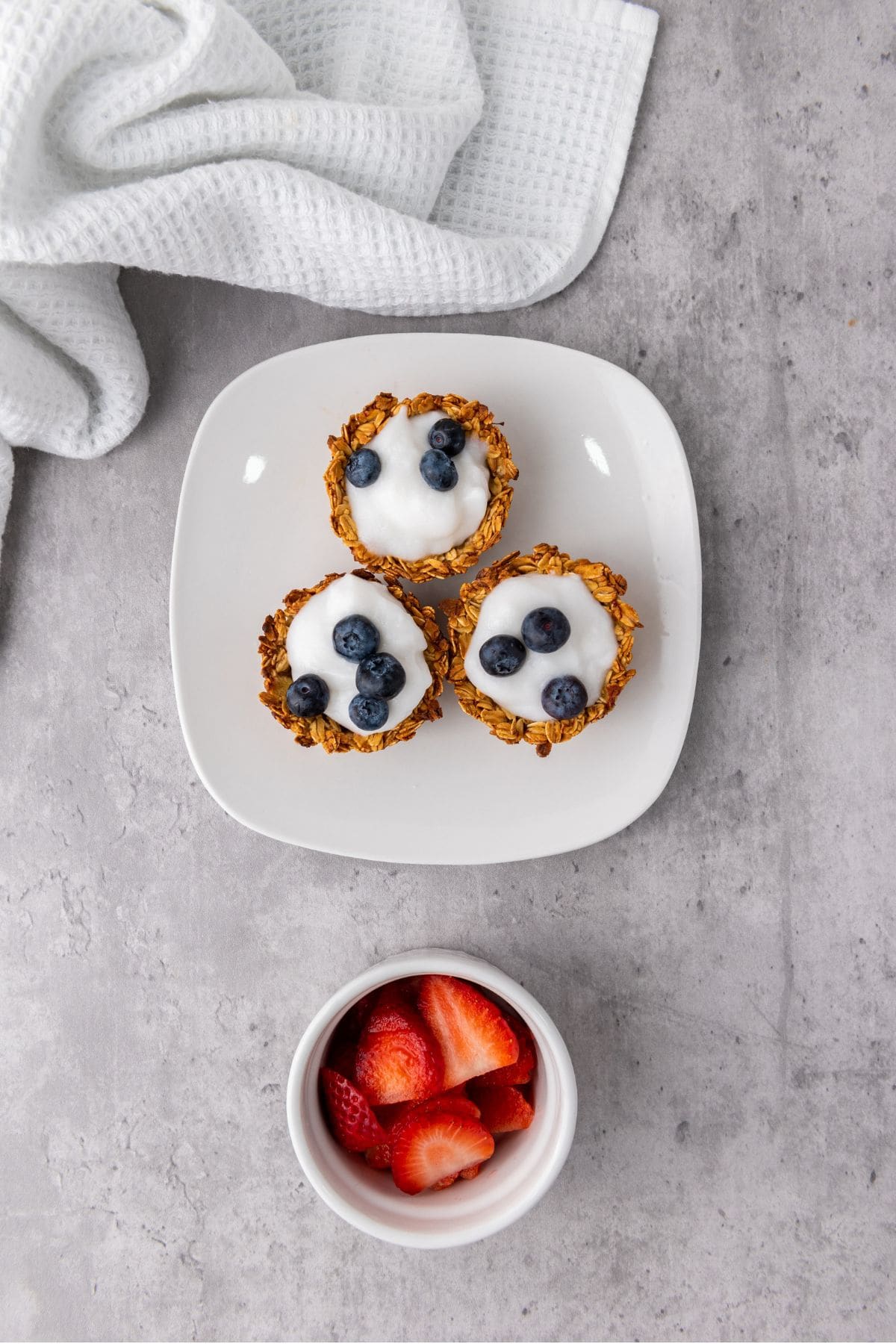Granola muffin cups being filled with creamy yogurt and topped with fresh berries.