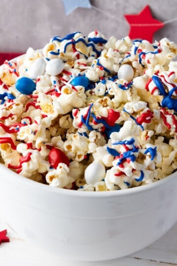 A bowl filled with patriotic popcorn, featuring clusters coated in red, white, and blue candy melts with festive sprinkles.