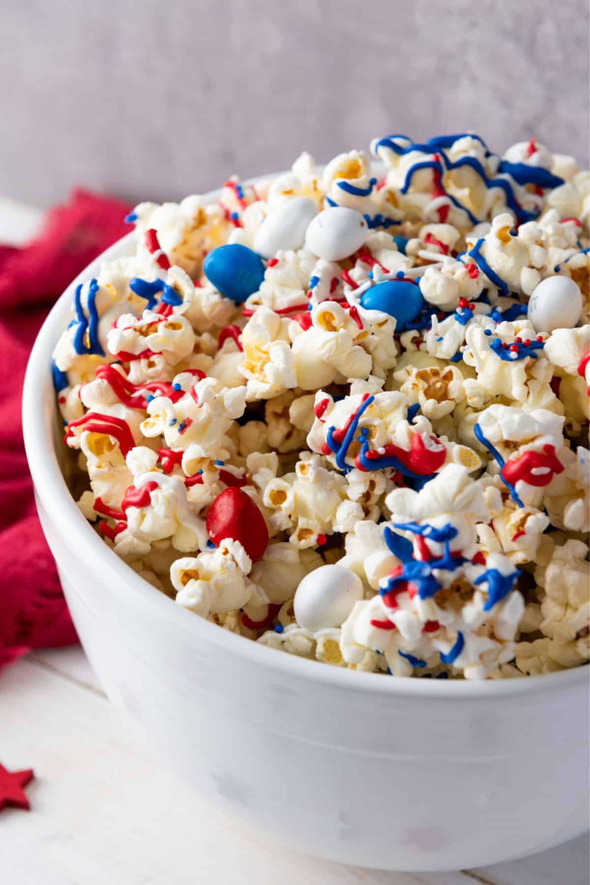 A bowl filled with patriotic popcorn, generously coated with red, white, and blue candies and sprinkles.