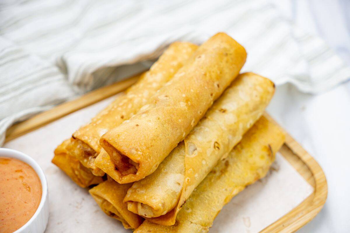 Close-up photo of crispy, golden-brown spring rolls stacked on a wooden board.
