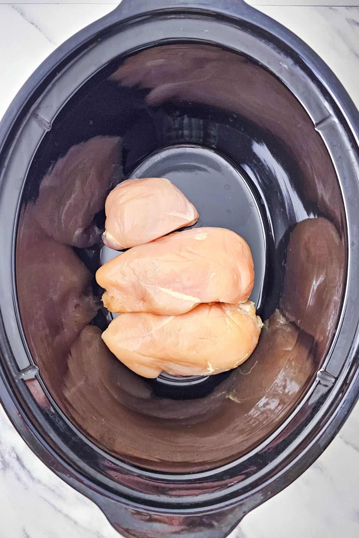 Chicken breasts placed in a crockpot.