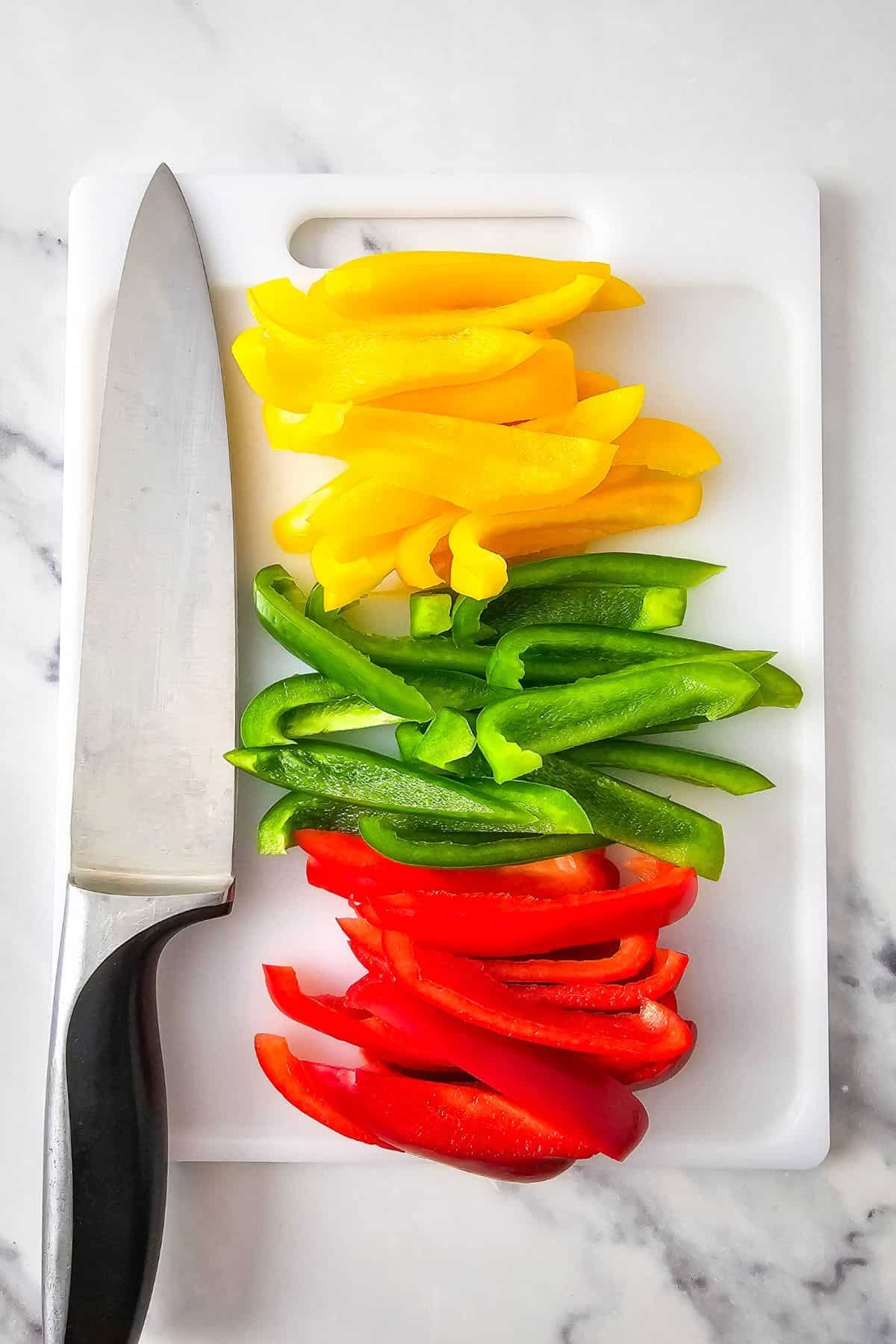 Chopped red, yellow, and green bell peppers on a chopping board.