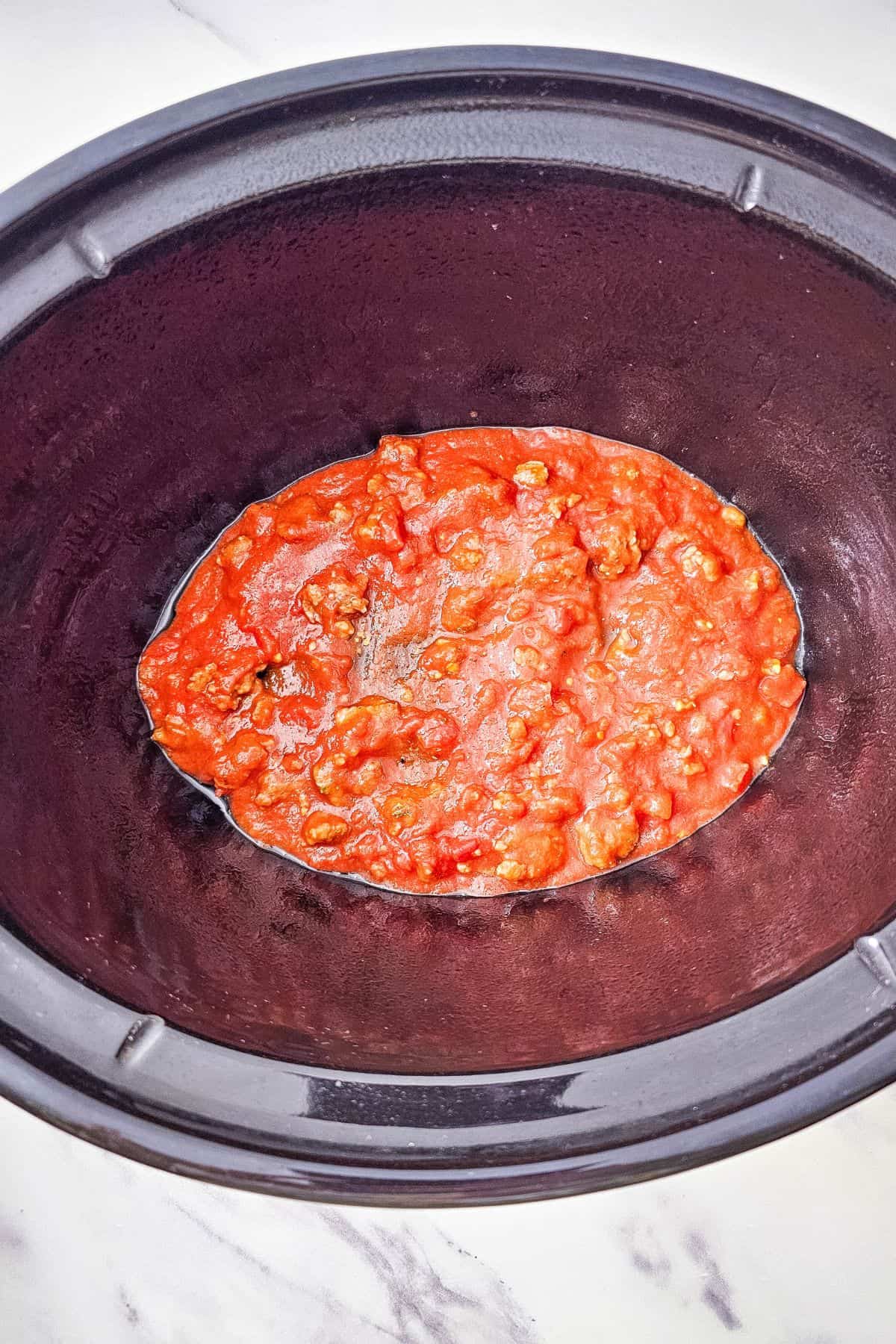 A thin layer of sauce mixture spread across the bottom of the slow cooker.