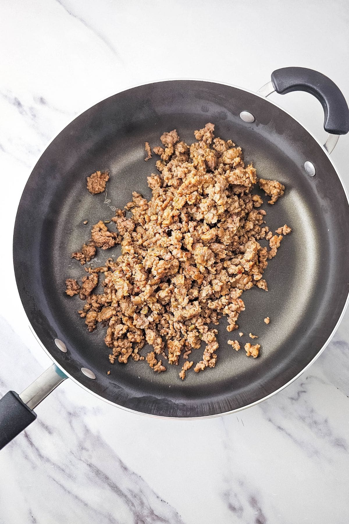 Italian sausage browning in a pan, with small crumbles forming as it cooks.