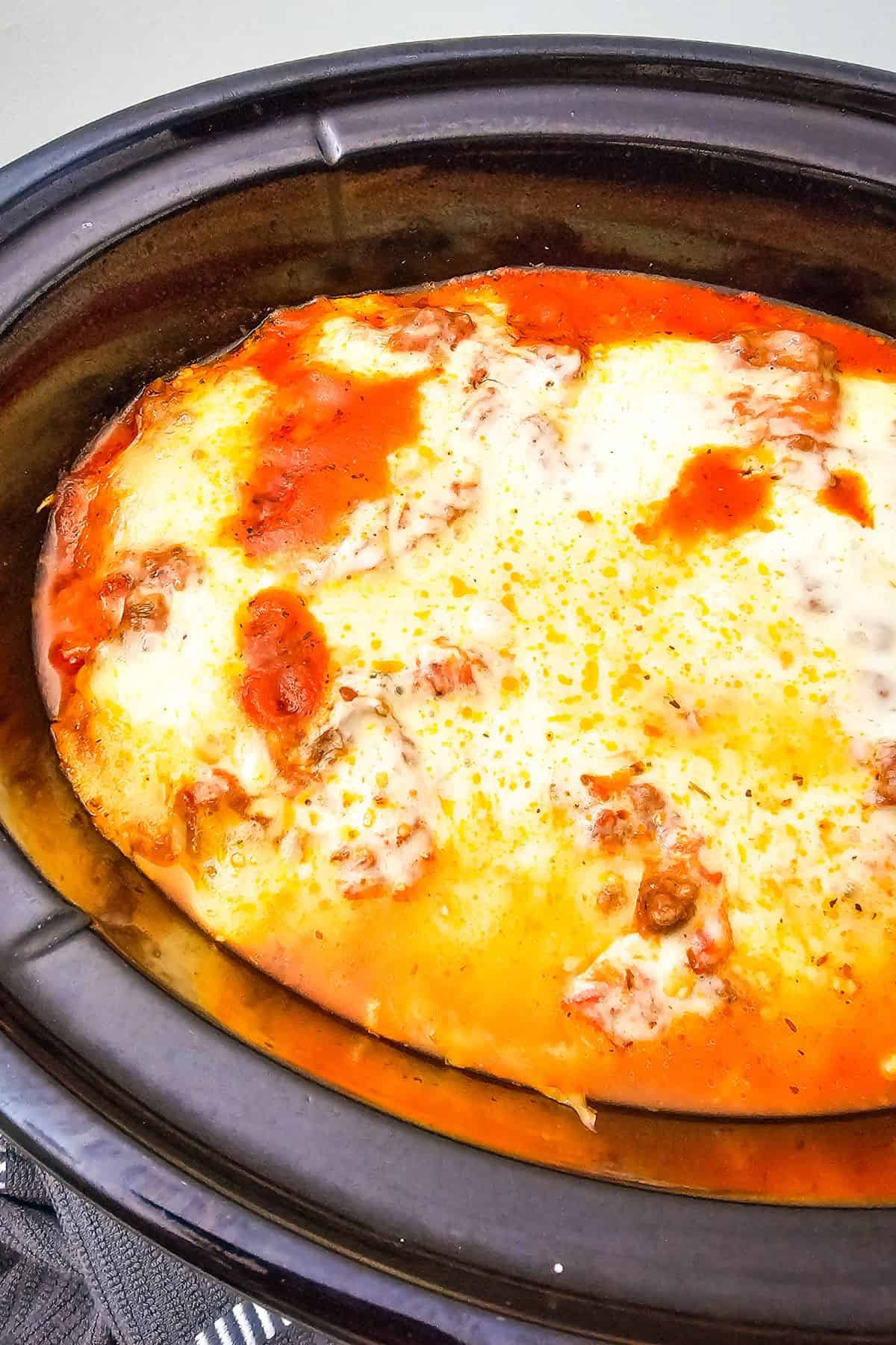 Lasagna fully cooked in the crockpot, with melted, golden cheese on top.