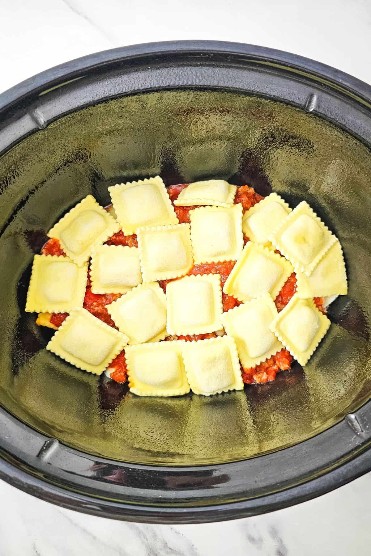 Lasagna layered in the crockpot, topped with ravioli.