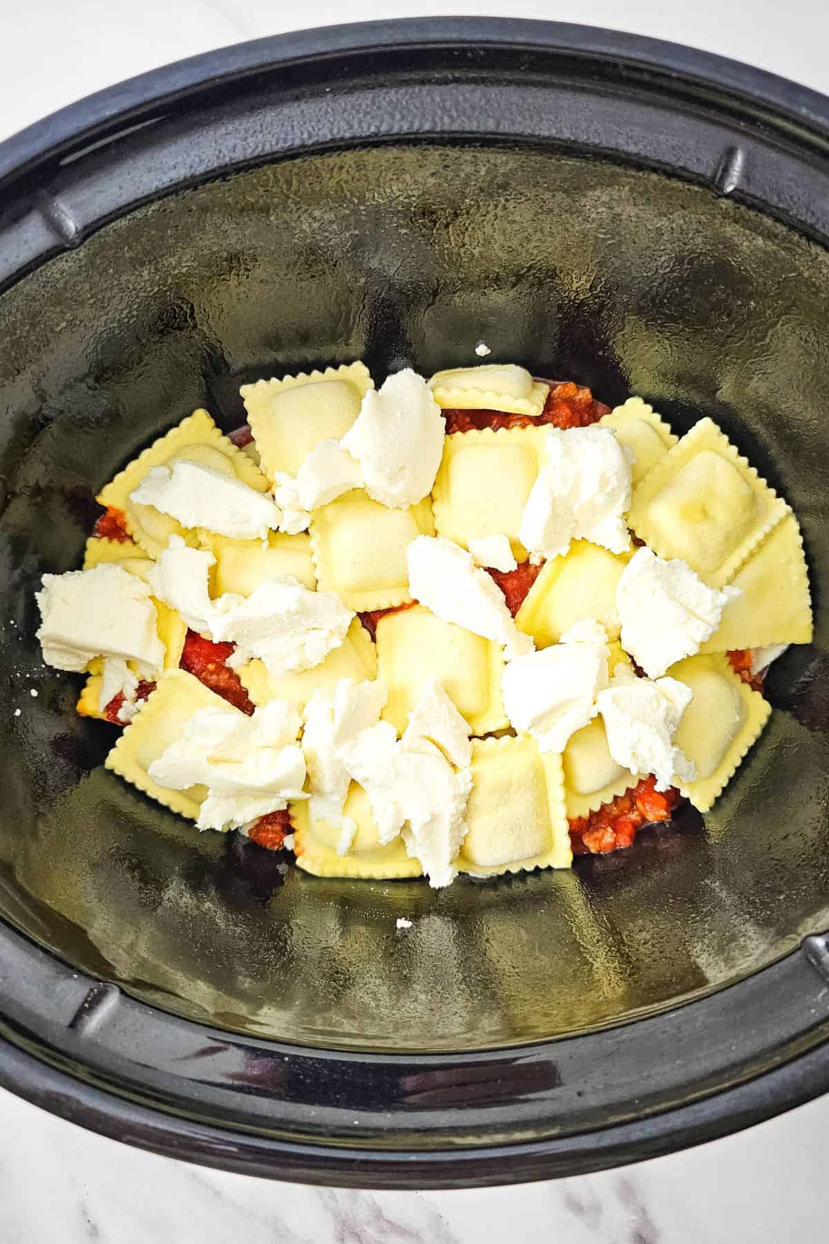 Lasagna layered in the crockpot, topped with cheese, ready to be cooked.