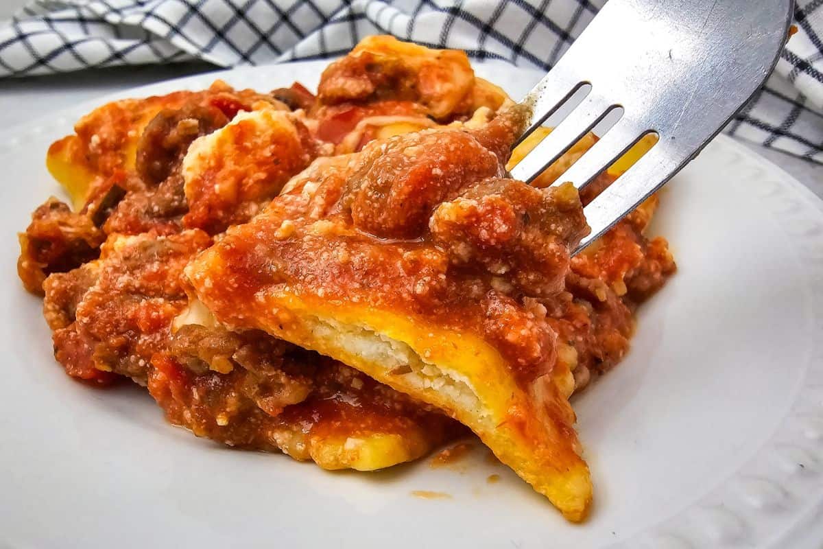 Close-up of lasagna being served on a plate, with a fork lifting a portion, showing layers of pasta, sauce, and melted cheese.