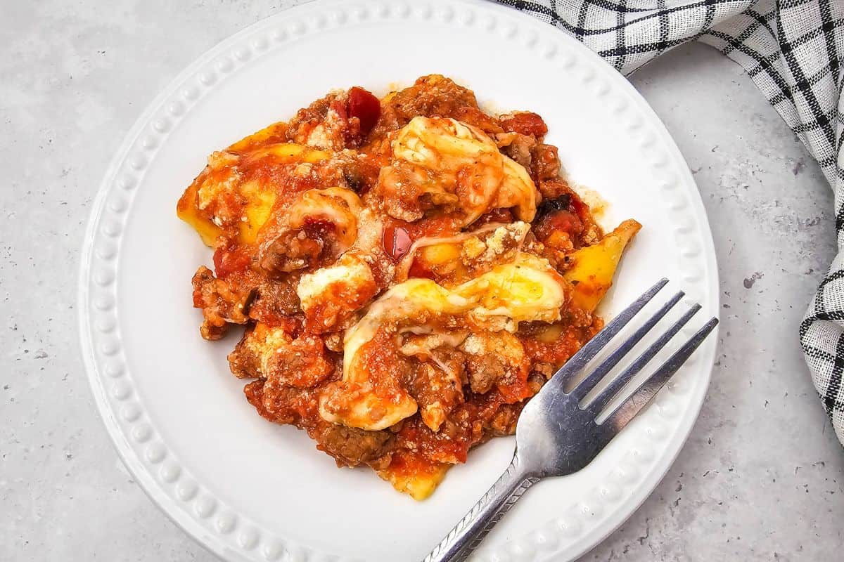 A plate of cheesy lasagna with golden mozzarella on top, served with a fork on the side.