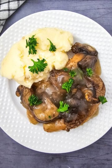 A plate of Crockpot Chicken Marsala with chicken, mushrooms, creamy sauce, and parsley, served with mashed potatoes.