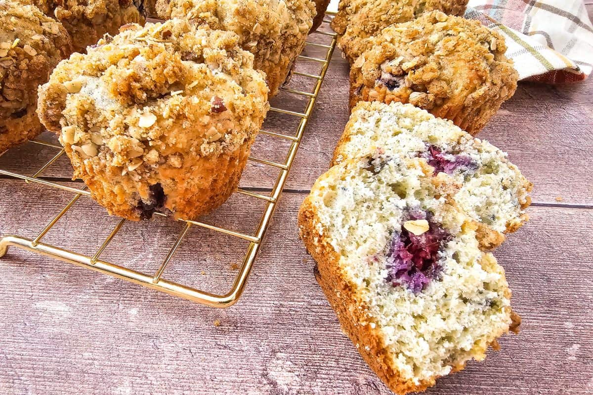 Muffins cooling on a wire rack, with one muffin broken open to display its moist interior.