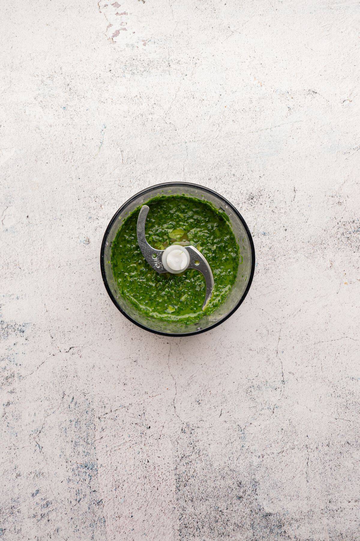 A blender with fresh basil, olive oil, lemon juice, and seasonings being mixed together.