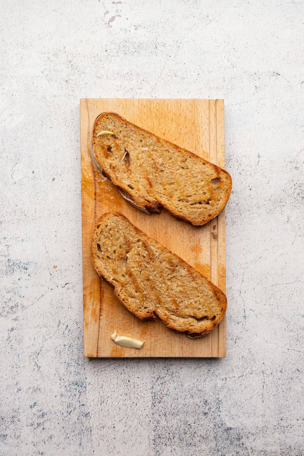 Two slices of bread spread with olive oil on a cutting board.
