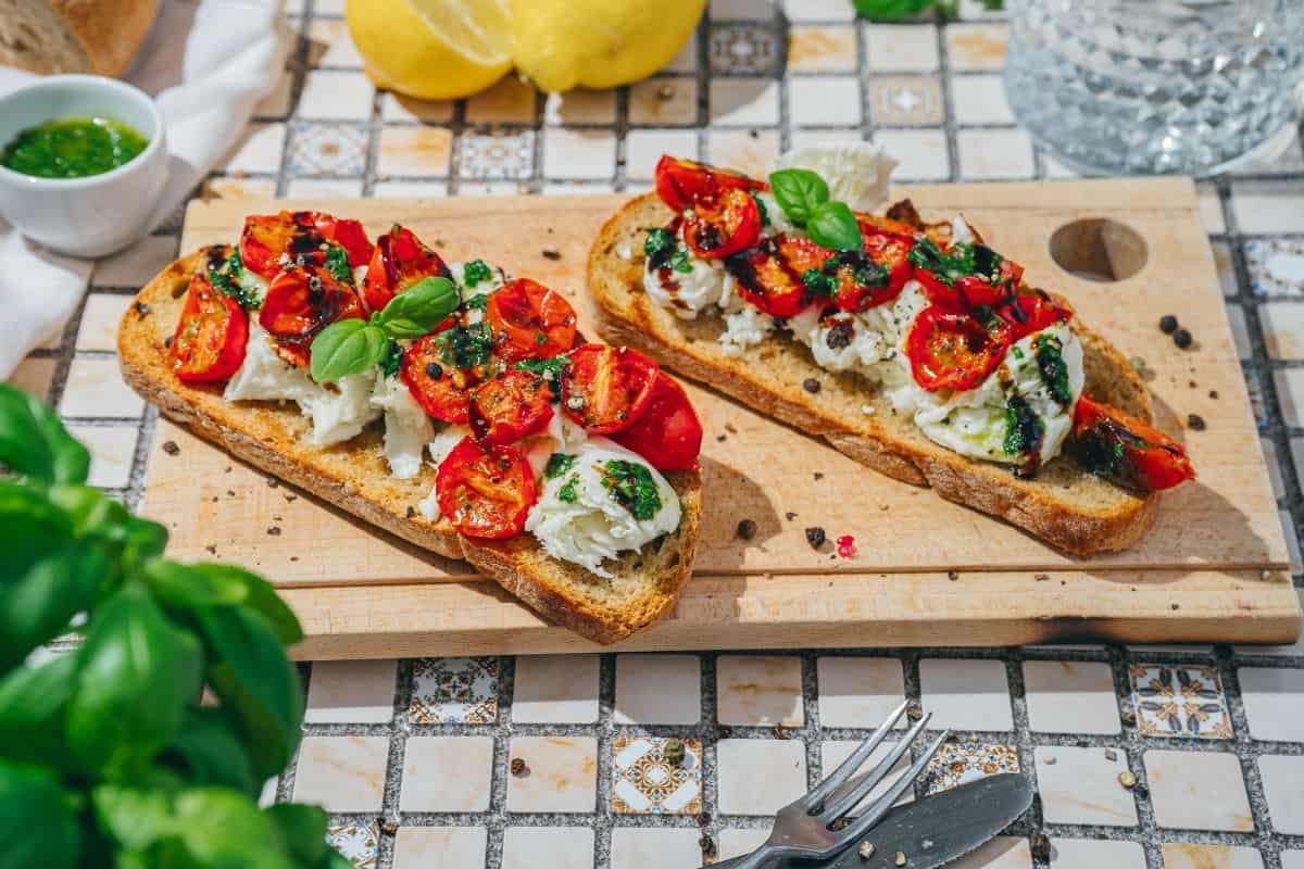 Two pieces of burrata toast on a plate, topped with roasted tomatoes, fresh basil, and a drizzle of basil sauce.