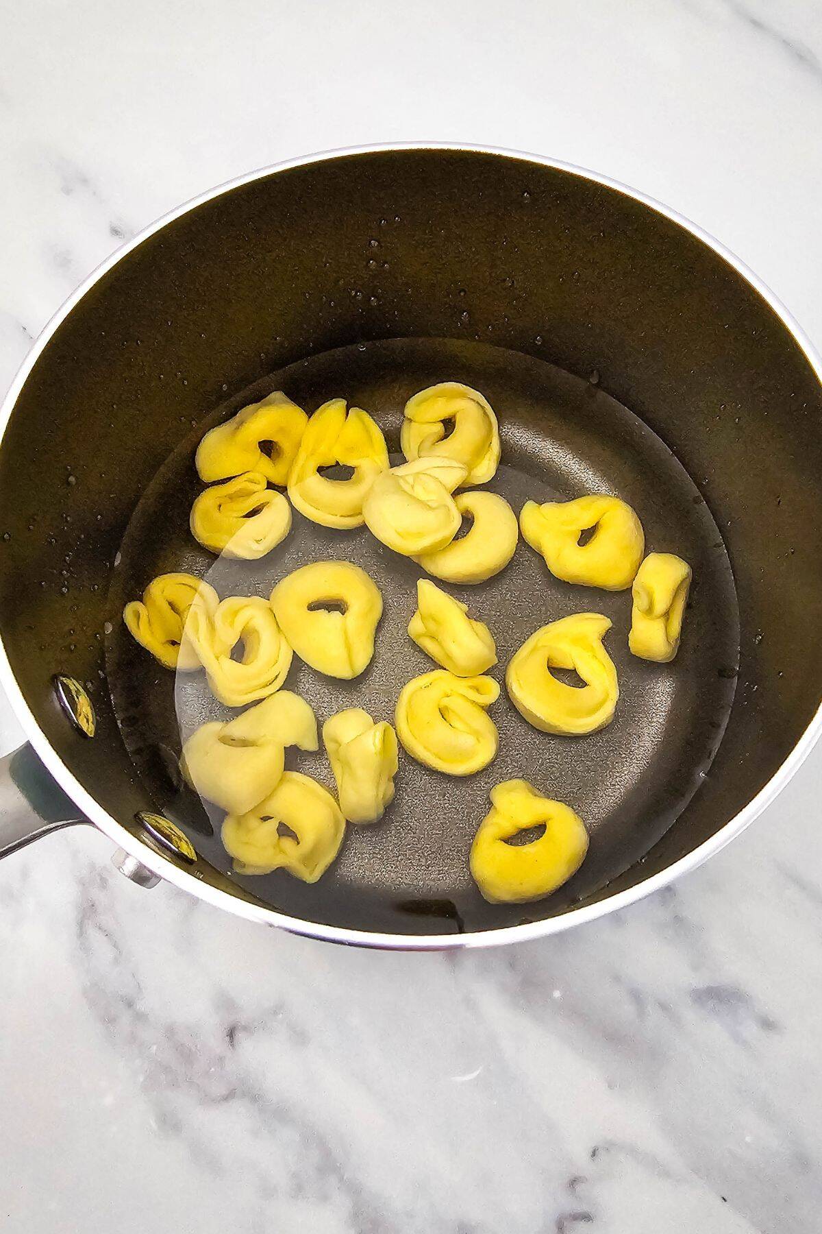 Cheese tortellini being added to a saucepan for cooking.