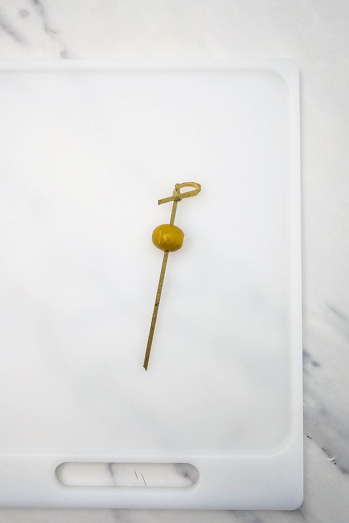 A green olive being threaded onto a skewer as the first ingredient.