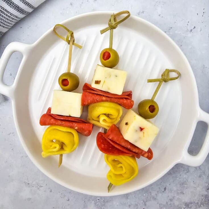 Three tortellini skewers on a plate, each with an olive, cheese cube, folded pepperoni, green tortellini, all neatly arranged.