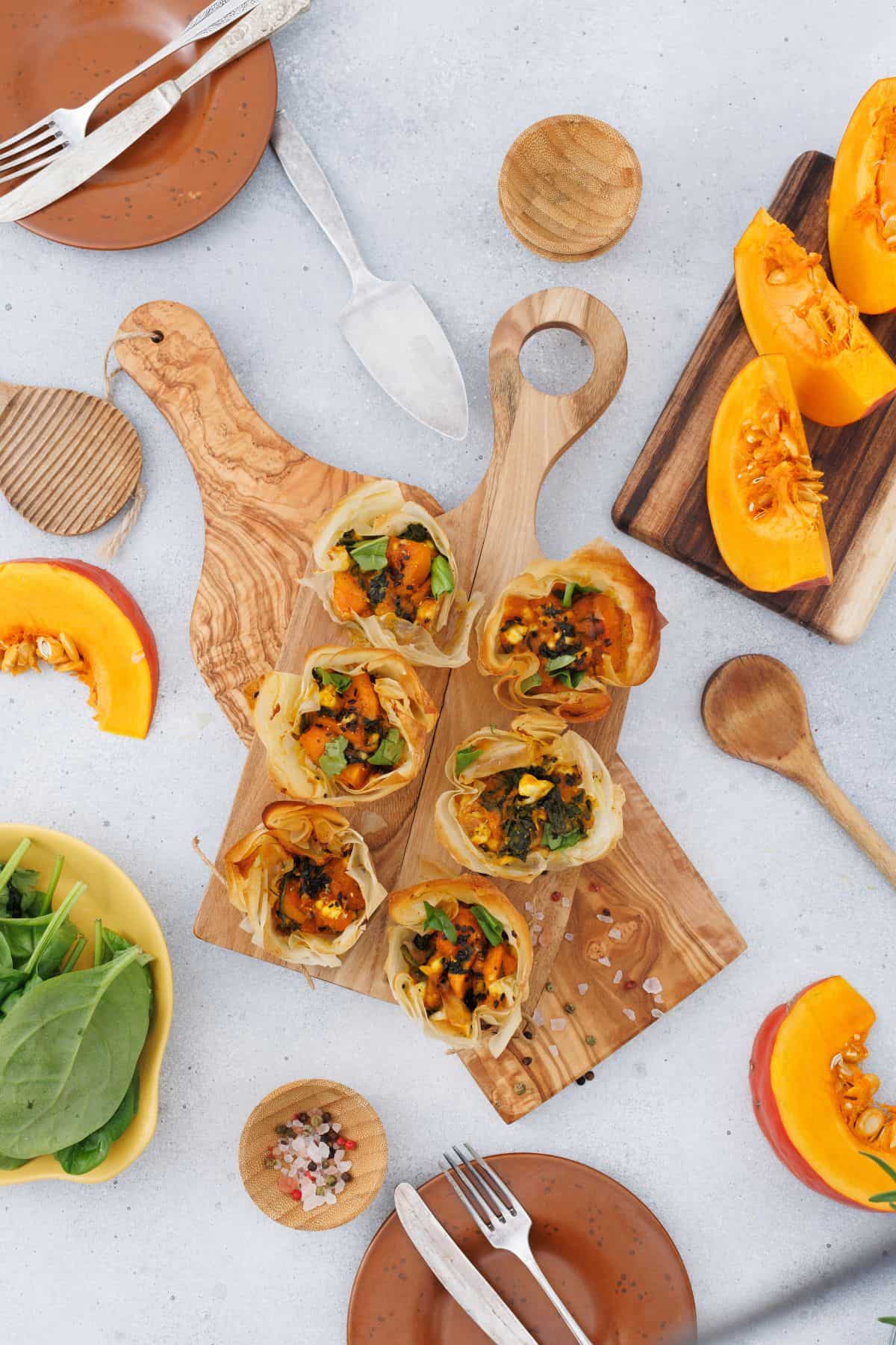 Pumpkin feta phyllo cups served on a wooden board, garnished with seeds, with a pumpkin and decorative items in the background.