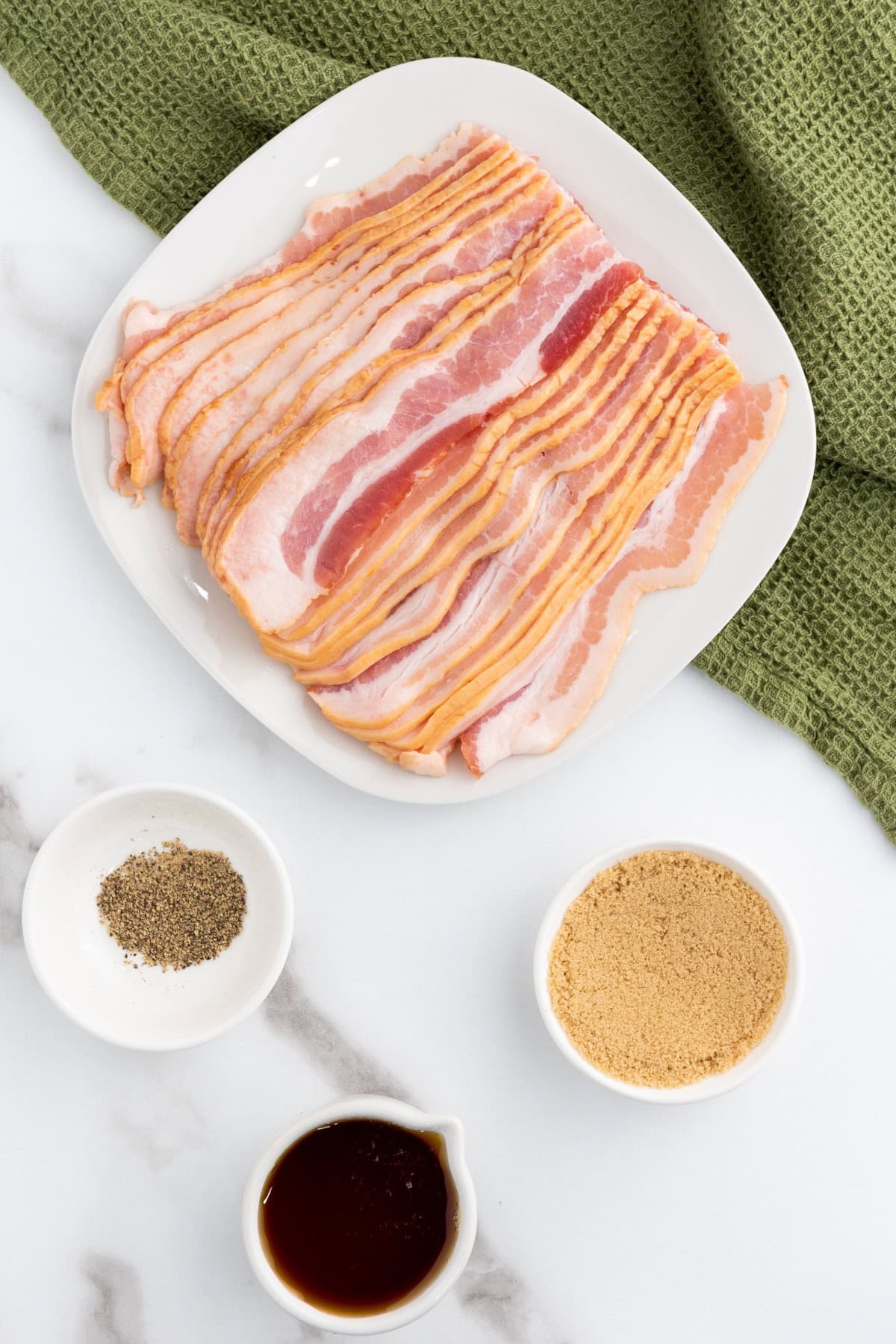 Ingredients for Candied Maple Brown Sugar Bacon, including bacon, maple syrup, brown sugar, and black pepper.