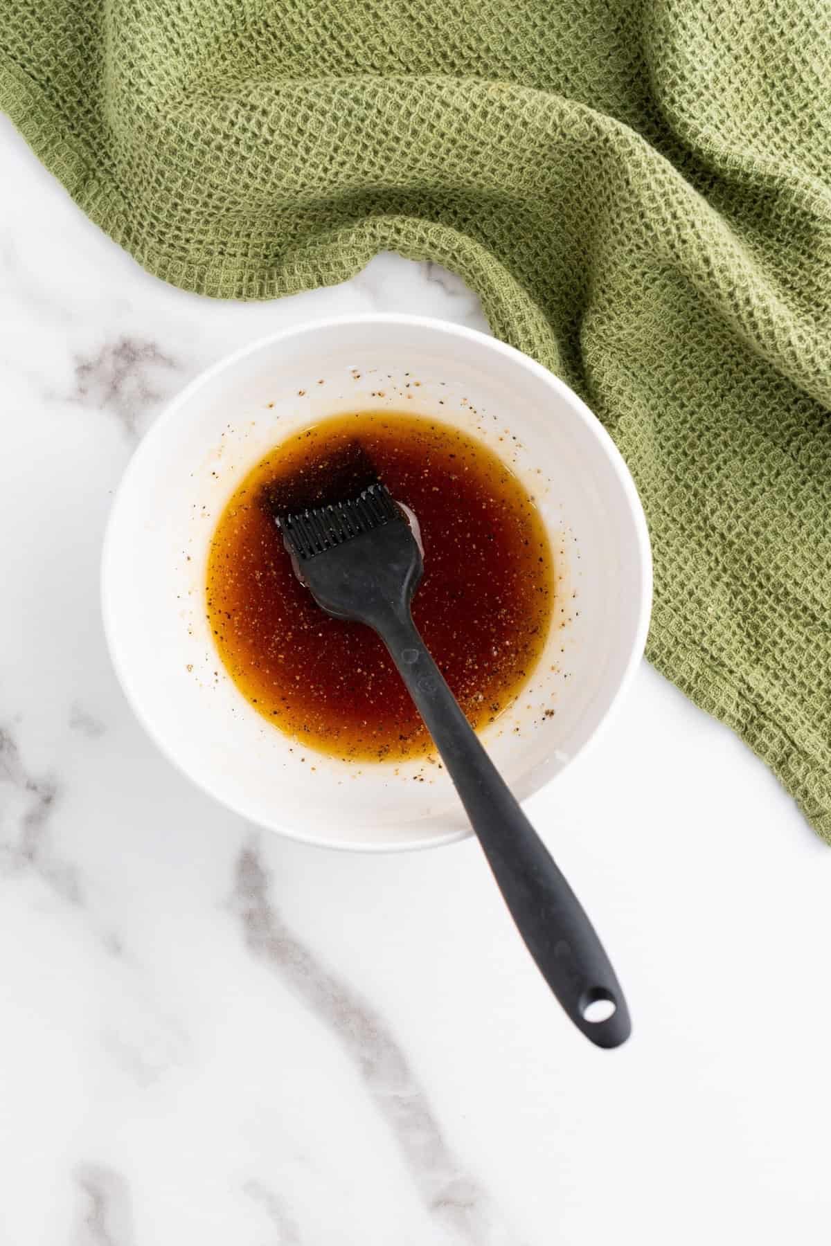 A small bowl filled with sauce mixture and a brush resting inside.