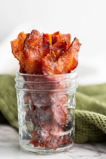 Candied maple brown sugar bacon in a small jar, with a green cloth in the background.