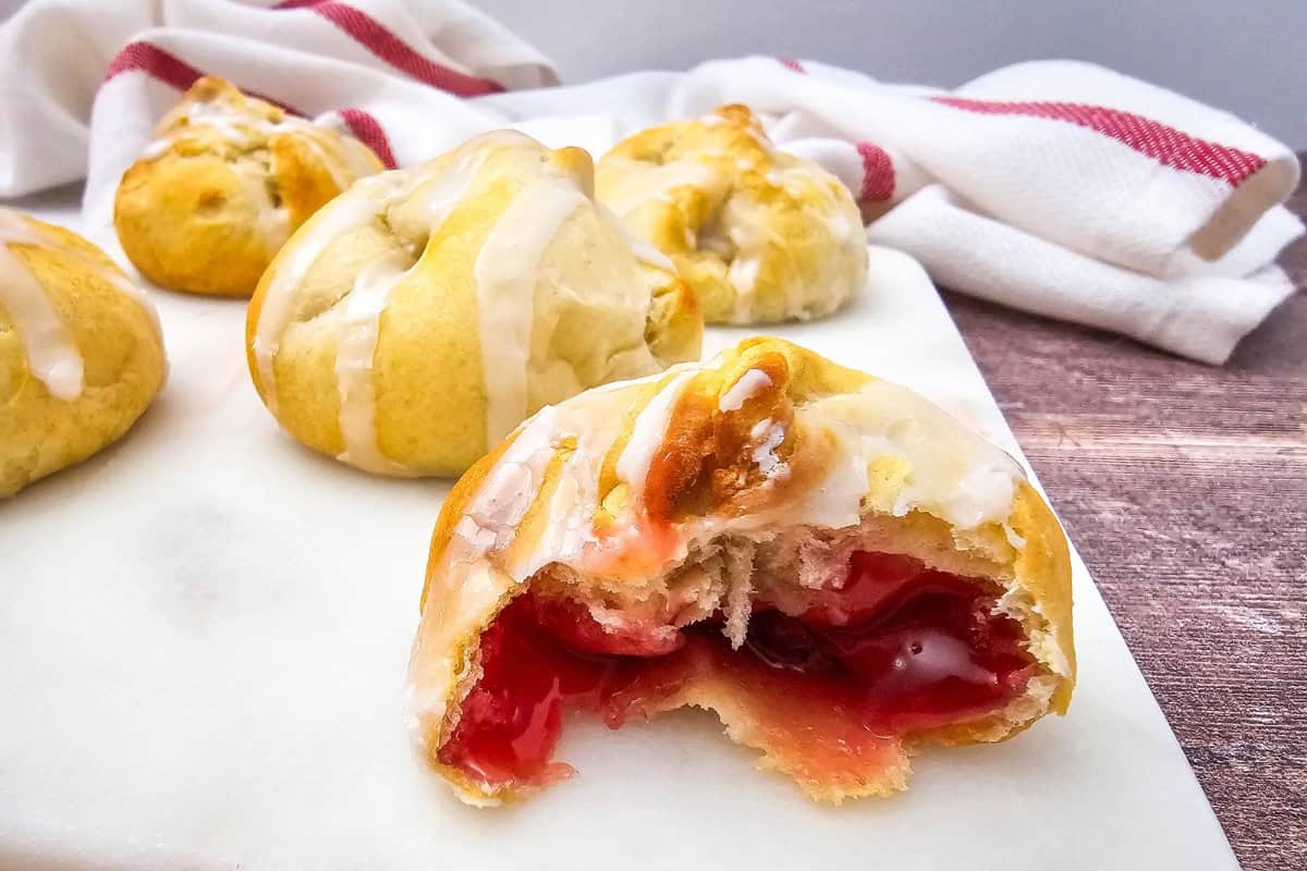 Close-up photo of a cherry pie bites lined up on a plate, with one piece showing a bite and cherry filling inside.