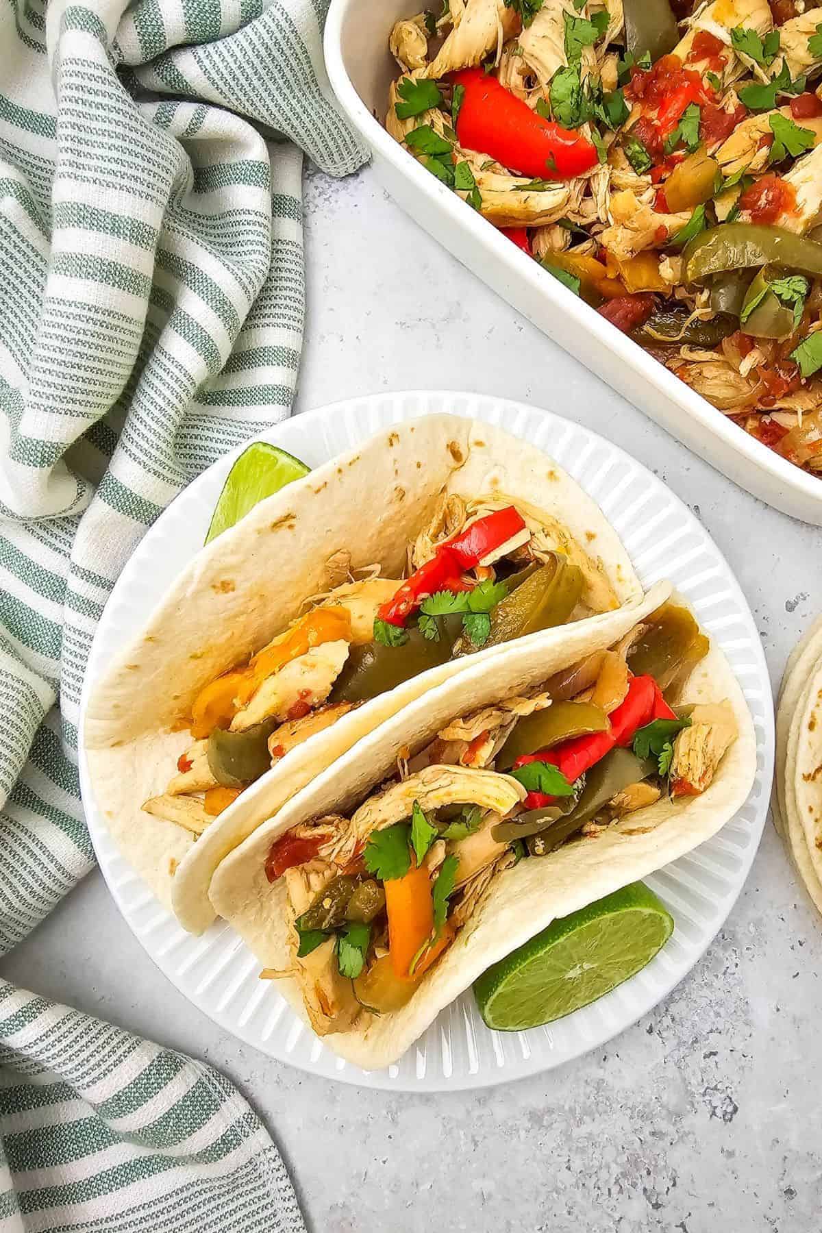 Two chicken fajitas served on a plate with colorful bell peppers and onions.