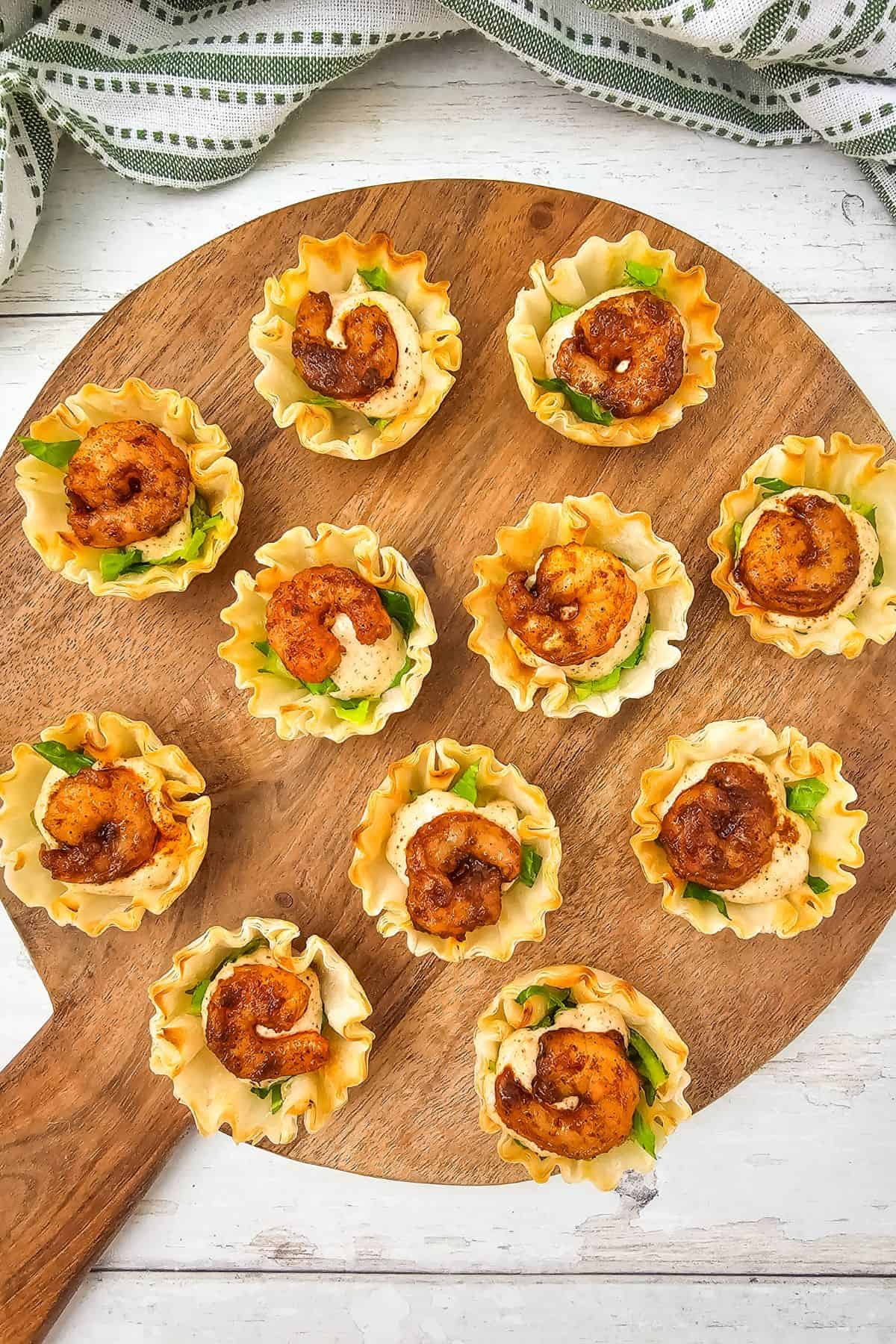 Chili Lime Shrimp Cups arranged on a wooden board with shrimp, sauce, and lettuce in phyllo shells.