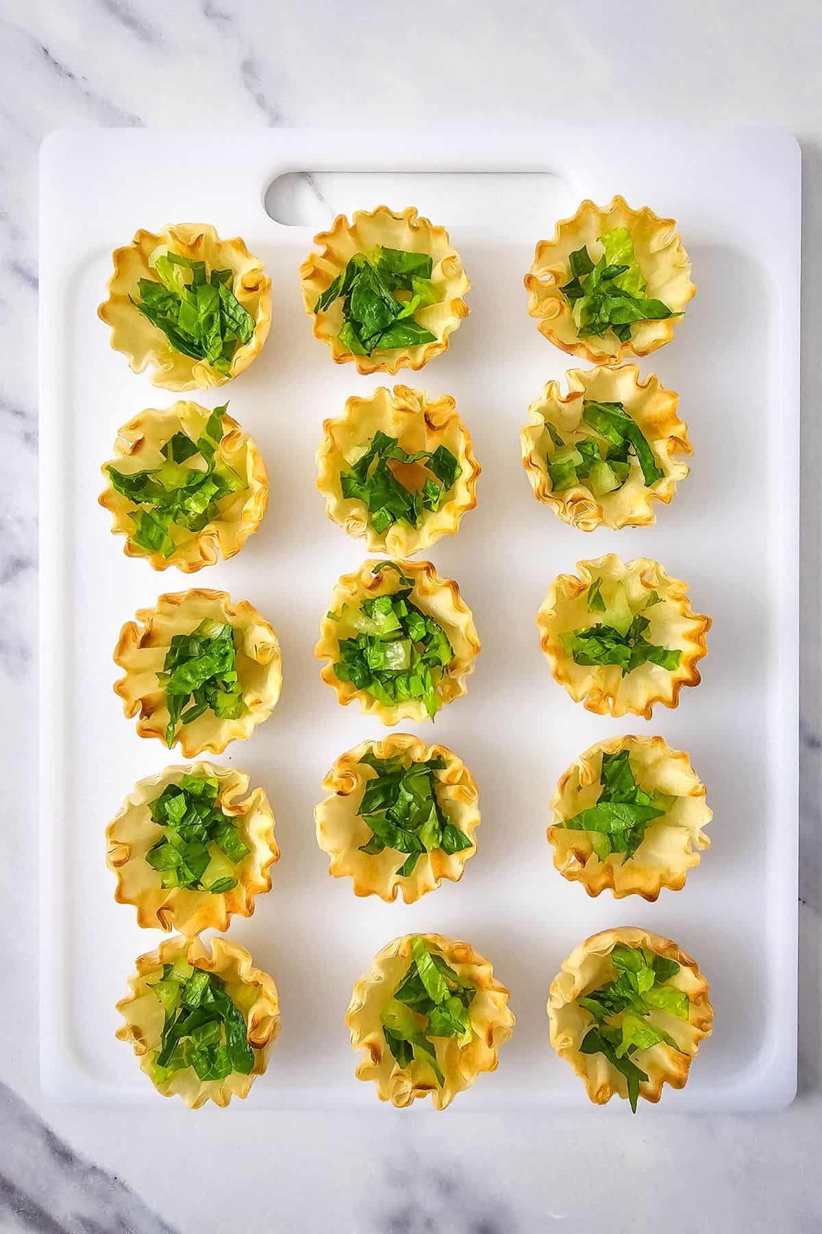 Shredded lettuce placed inside phyllo shells arranged on a serving dish.
