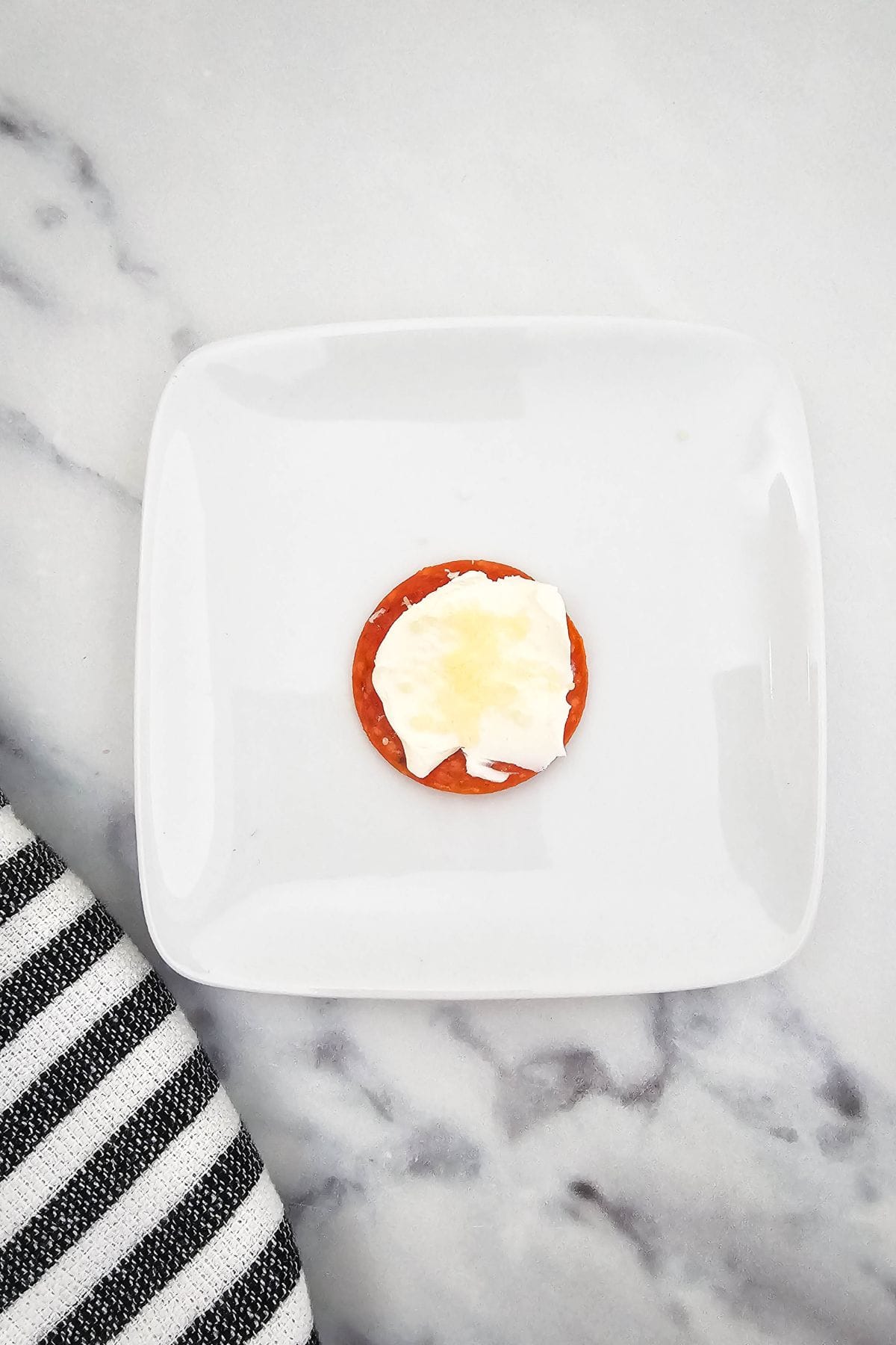 Single slice of pepperoni topped with cream cheese and grated parmesan on a plate.