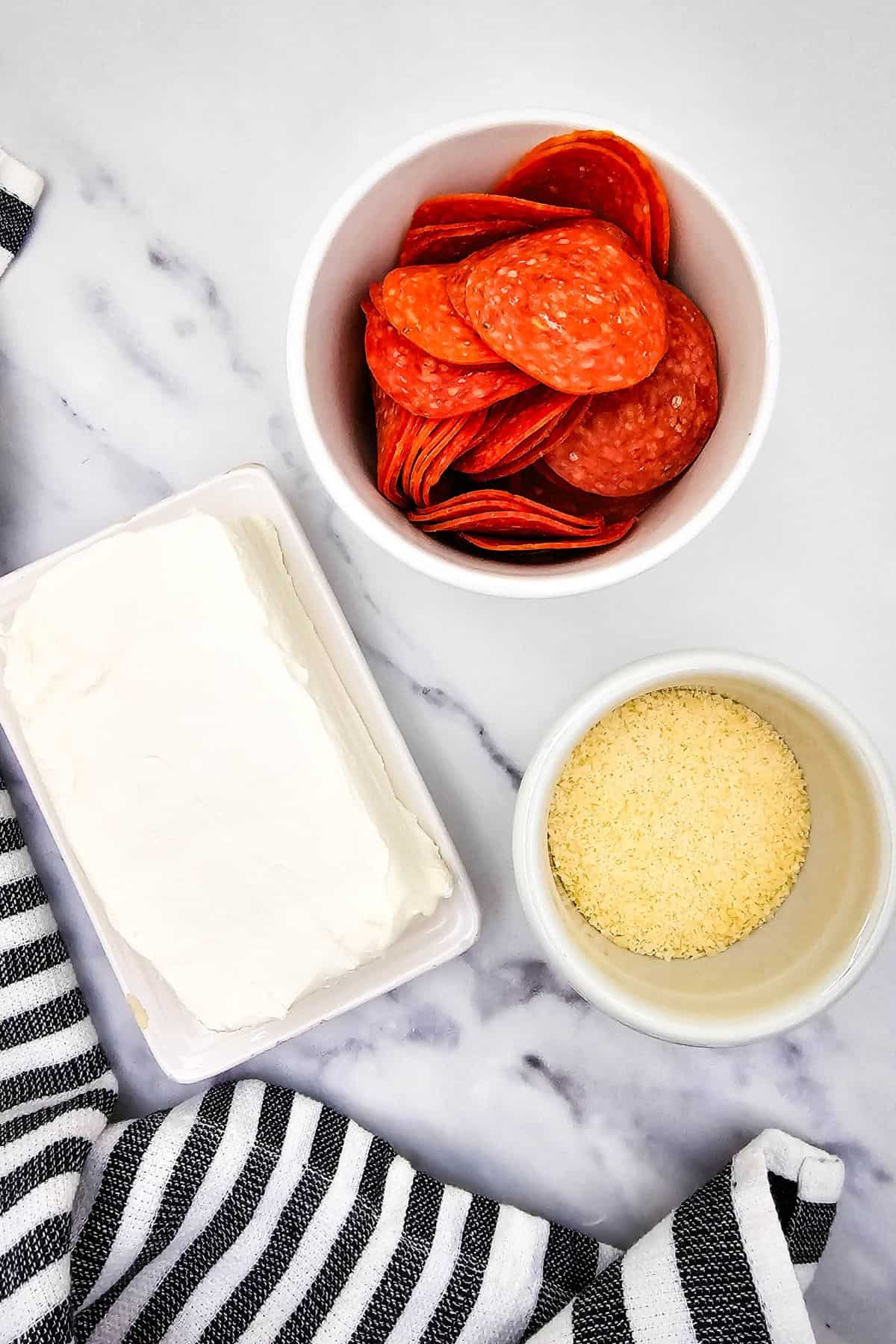 Ingredients such as pepperoni, cream cheese and parmesan arranged in a surface.